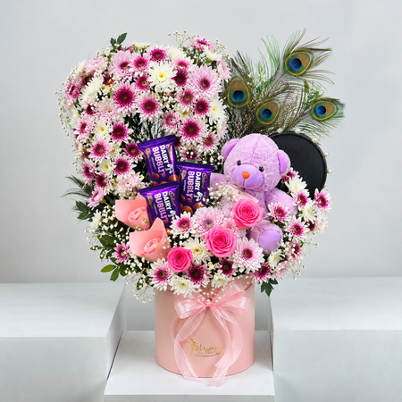 Heart-shaped pink chrysanthemum arrangement with teddy bear and peacock feathers in a pink box