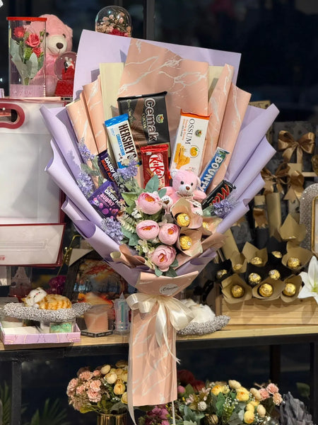Bouquet of flowers with candy and a teddy bear on a table.