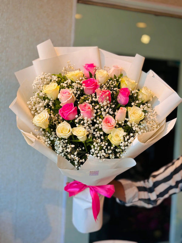 Bouquet of pink, yellow & white roses with baby's breath wrapped in white paper and a pink ribbon.