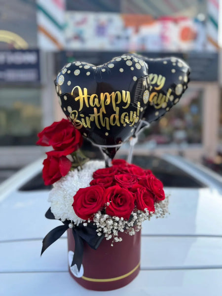 Birthday balloon arrangement with red and white flowers in a cup against a blurred background