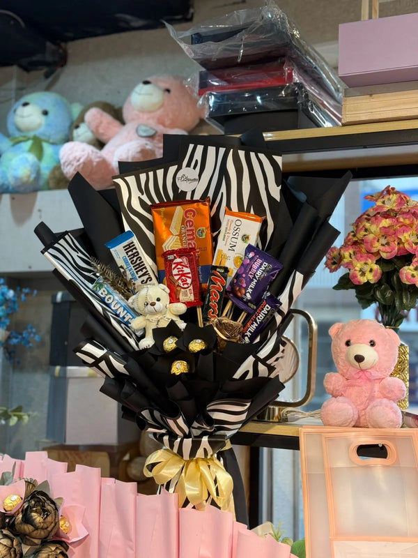 Bouquet of candy bars and small teddy bears with a zebra pattern ribbon, surrounded by more teddy bears and flowers.