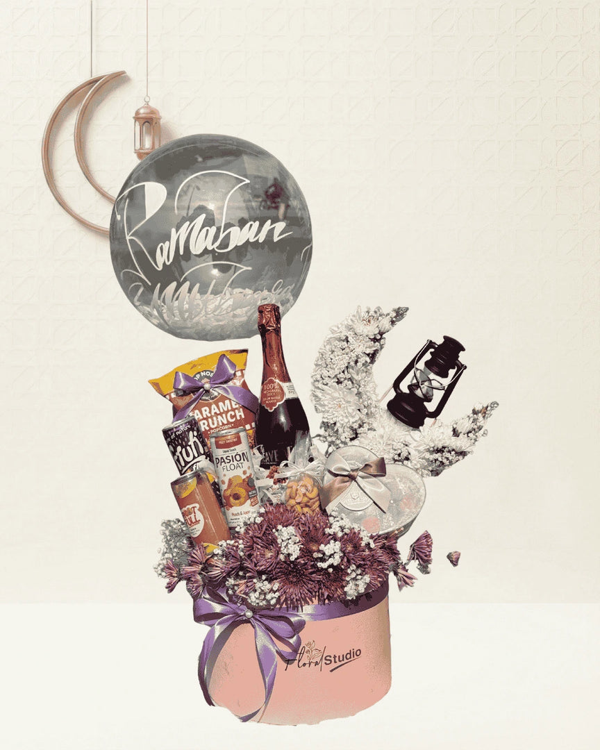 Gift basket with champagne, snacks, and flowers on a light background