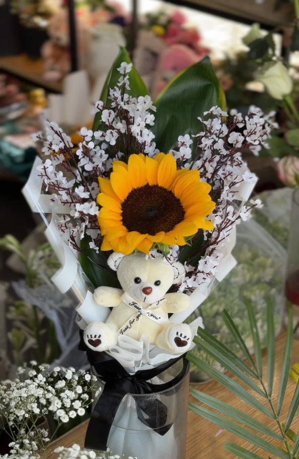 Bouquet with sunflower, teddy bear, and white flowers in a clear vase. Send flower to Pakistan.