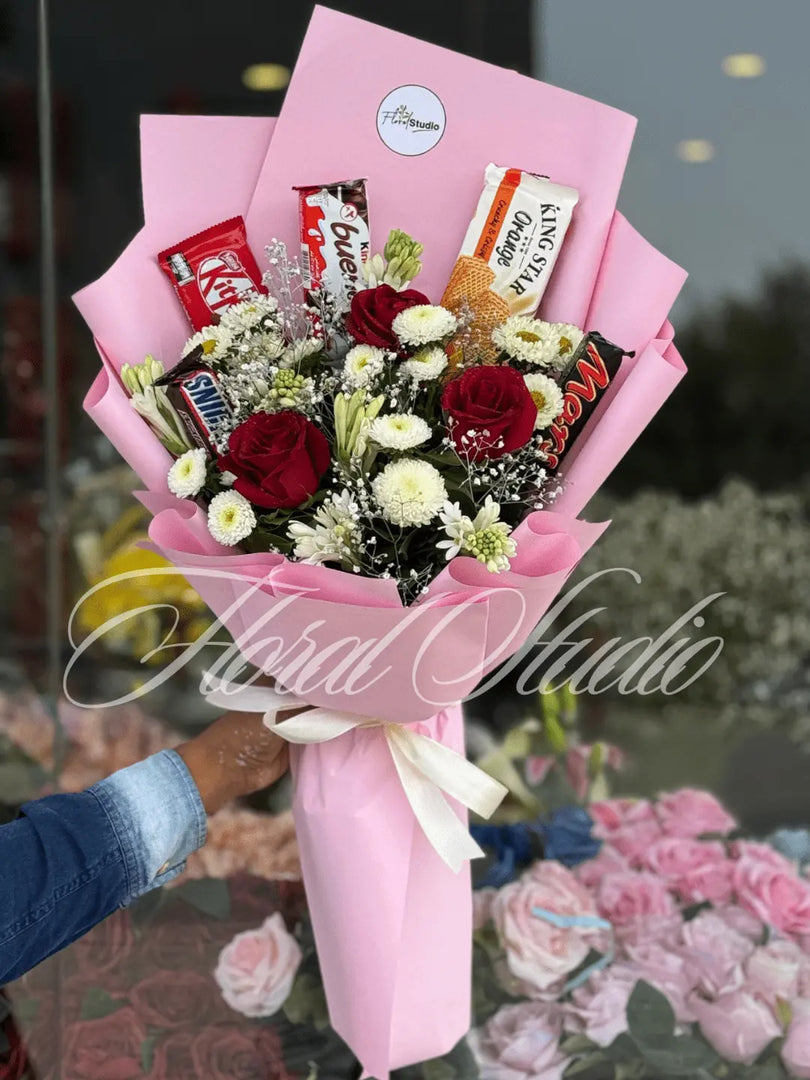 Bouquet of flowers with Kit Kat bars wrapped in pink paper, held by a person. Send flowers to lahore.