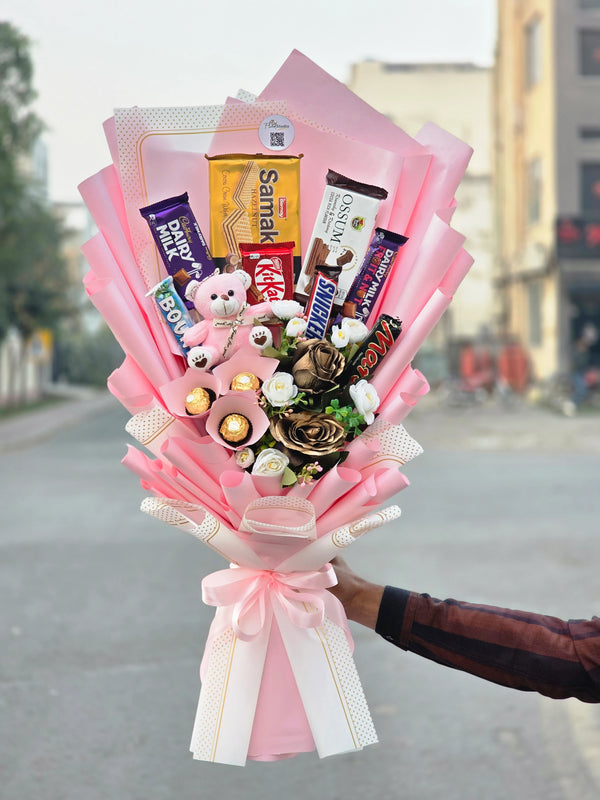 Bouquet of candy bars and a teddy bear held by a person on a street.