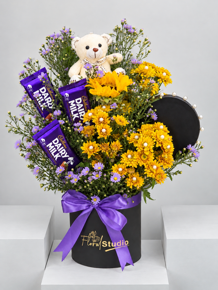 Yellow chrysanthemums and sunflower with Dairy Milk bars and a teddy bear in a black box