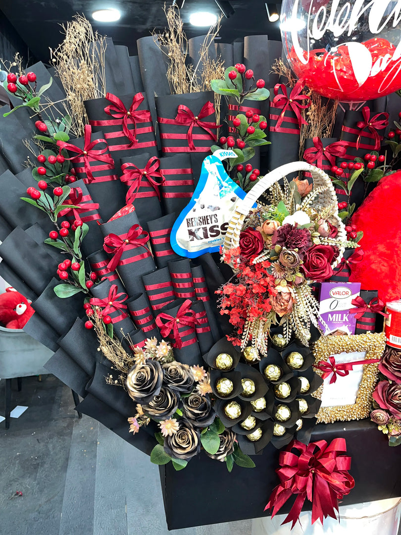 Decorative wreath with flowers, chocolates, and gift boxes on a stand.