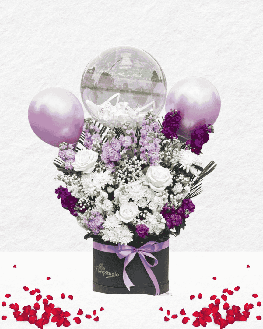 Floral arrangement with balloons and a black box on a light gray background