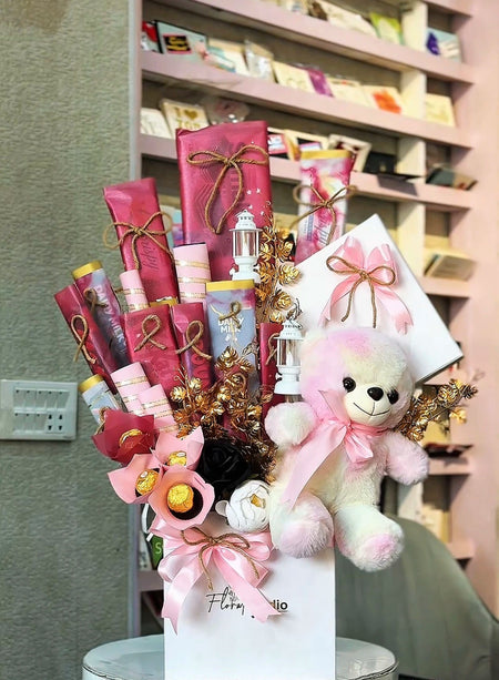 Bouquet of gifts including a teddy bear, flowers, and wrapped items in a store setting. Send flower to Pakistan.