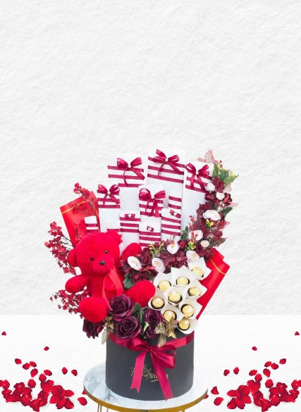 Decorative arrangement with flowers, a teddy bear, and wrapped gifts on a white background