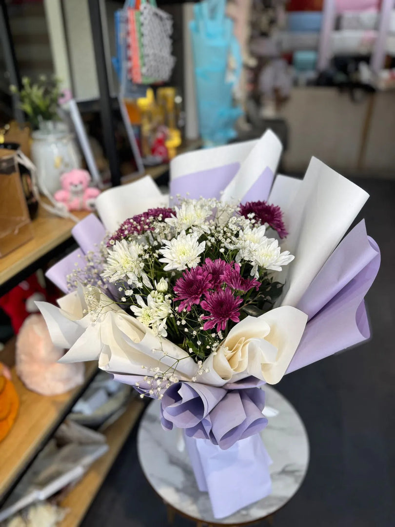 Bouquet of flowers with purple and white tones on a table in a store setting.