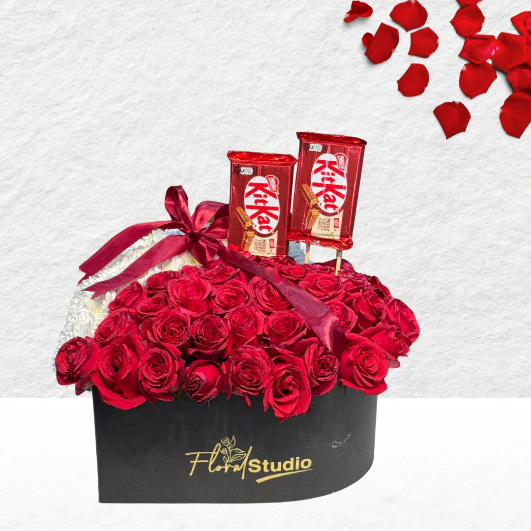 Black box filled with red roses, KitKat chocolate bars, and rose petals on a white background.