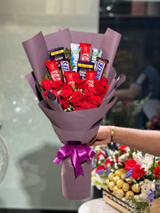 Bouquet of red roses and assorted candy bars wrapped in purple paper with a pink bow. Send flowers to lahore