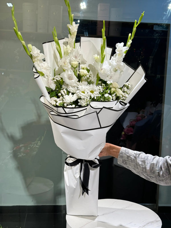 Bouquet of white chrysanthemums flowers wrapped in white paper with a black ribbon, held by a person.