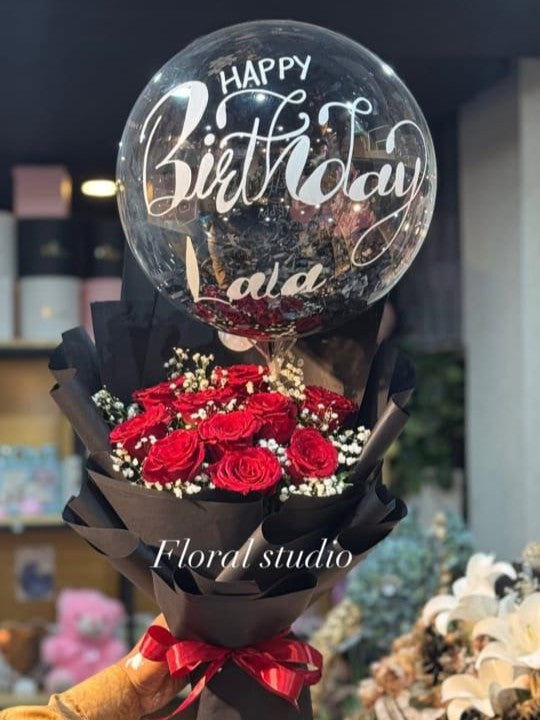 Bouquet of red roses with a transparent balloon displaying 'Happy Birthday' text, held by a person.