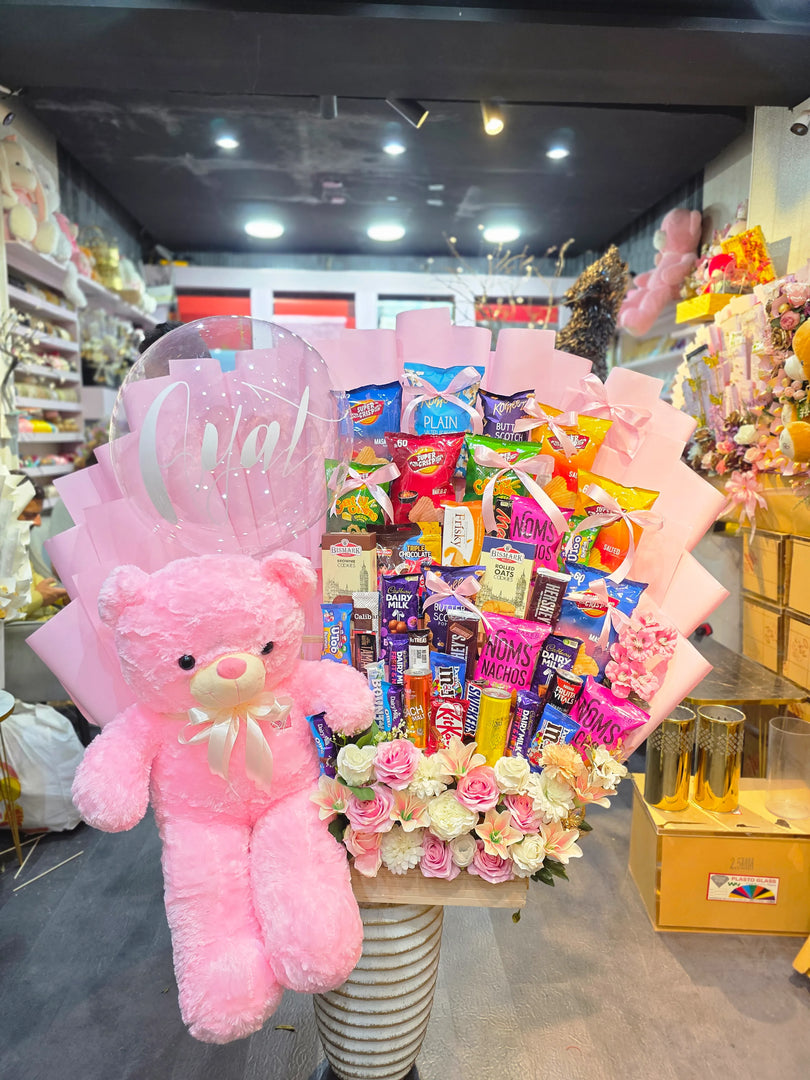Giant pink teddy bear, flowers, and assorted candies in a decorative arrangement with 'Giant' sign.
