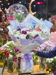 Bouquet of flowers with a teddy bear and a card in a store setting