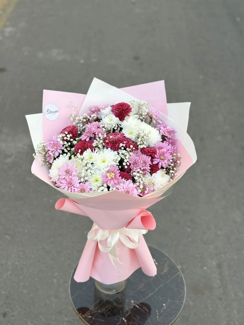 Bouquet of flowers wrapped in pink paper on a reflective surface with a gray background