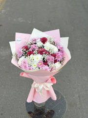 Bouquet of flowers wrapped in pink paper on a reflective surface with a gray background