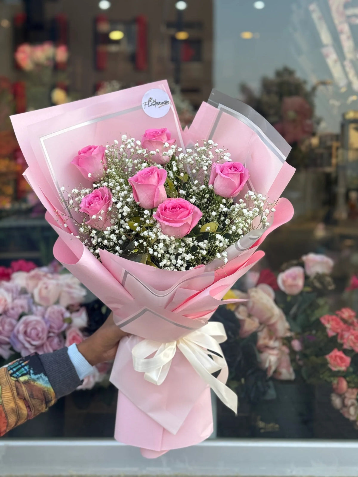 Bouquet of pink roses with baby's breath wrapped in pink paper and a white ribbon.
