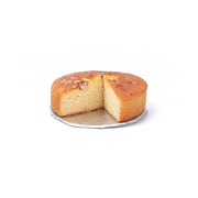 Round plain cake with one slice cut out on metal cooling rack against white background