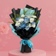 Bouquet of flowers wrapped in black paper with blue accents on a pink platform against a pink background with floral decorations.