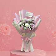 Bouquet of flowers wrapped in white paper with a 'Happy Birthday' card on a pink platform against a pink background.