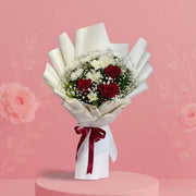 Bouquet of flowers wrapped in white paper with a red ribbon on a pink platform against a pink background.