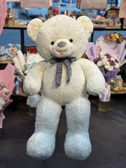 Large white teddy bear with a bow tie in a store setting