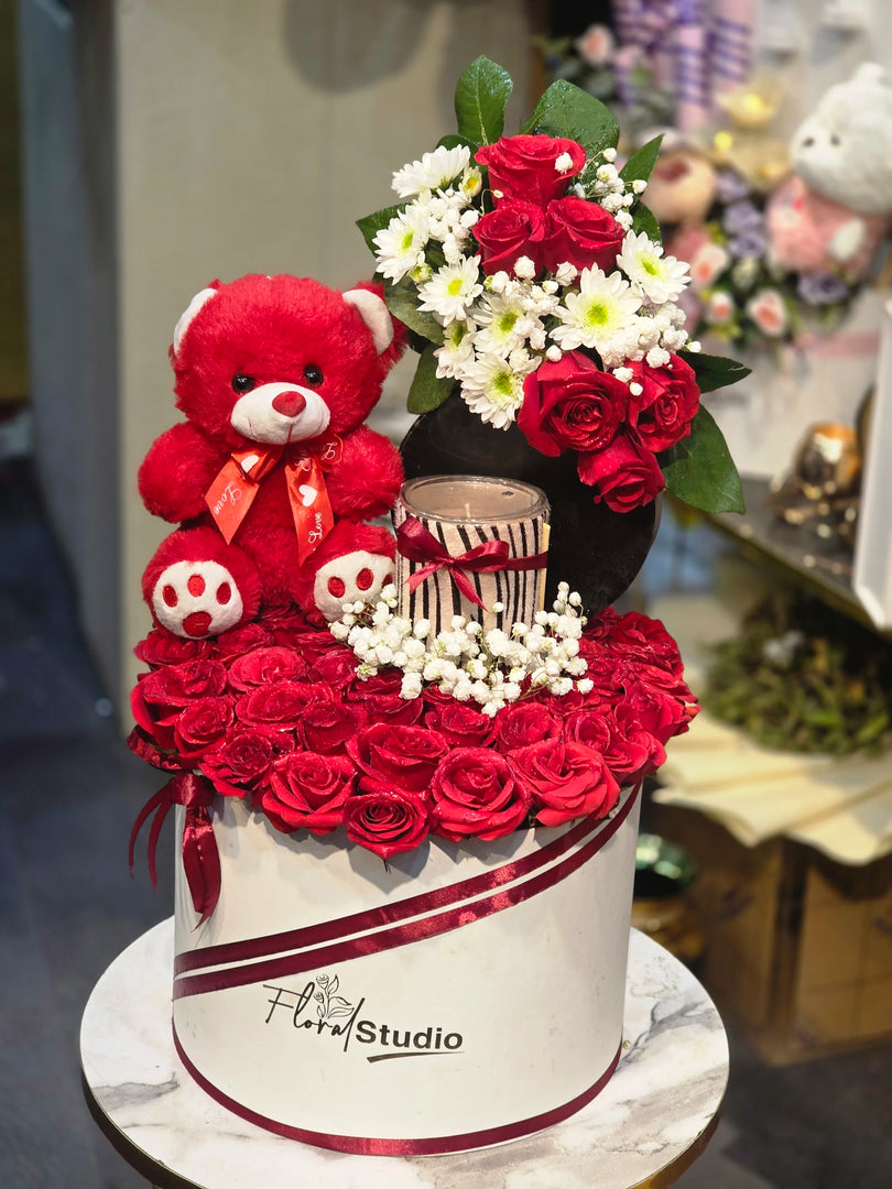 Decorative cake with red roses, a teddy bear, and flowers on a blurred background