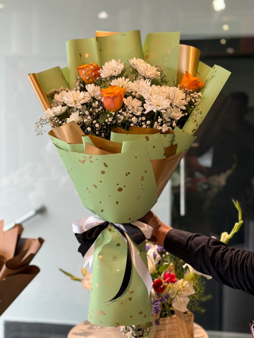 Bouquet of while chrysanthemums flowers wrapped in green paper with a black ribbon, held by a person.