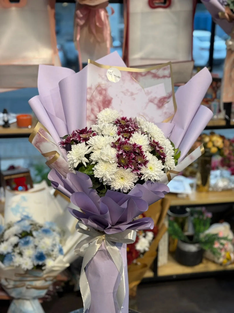 Bouquet of flowers wrapped in purple paper with a decorative card in a store setting.