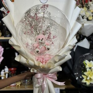 Pink teddy bear inside a clear balloon with baby’s breath flowers, wrapped in elegant white paper and pink ribbon — the Bloom Bear Balloon Bouquet.