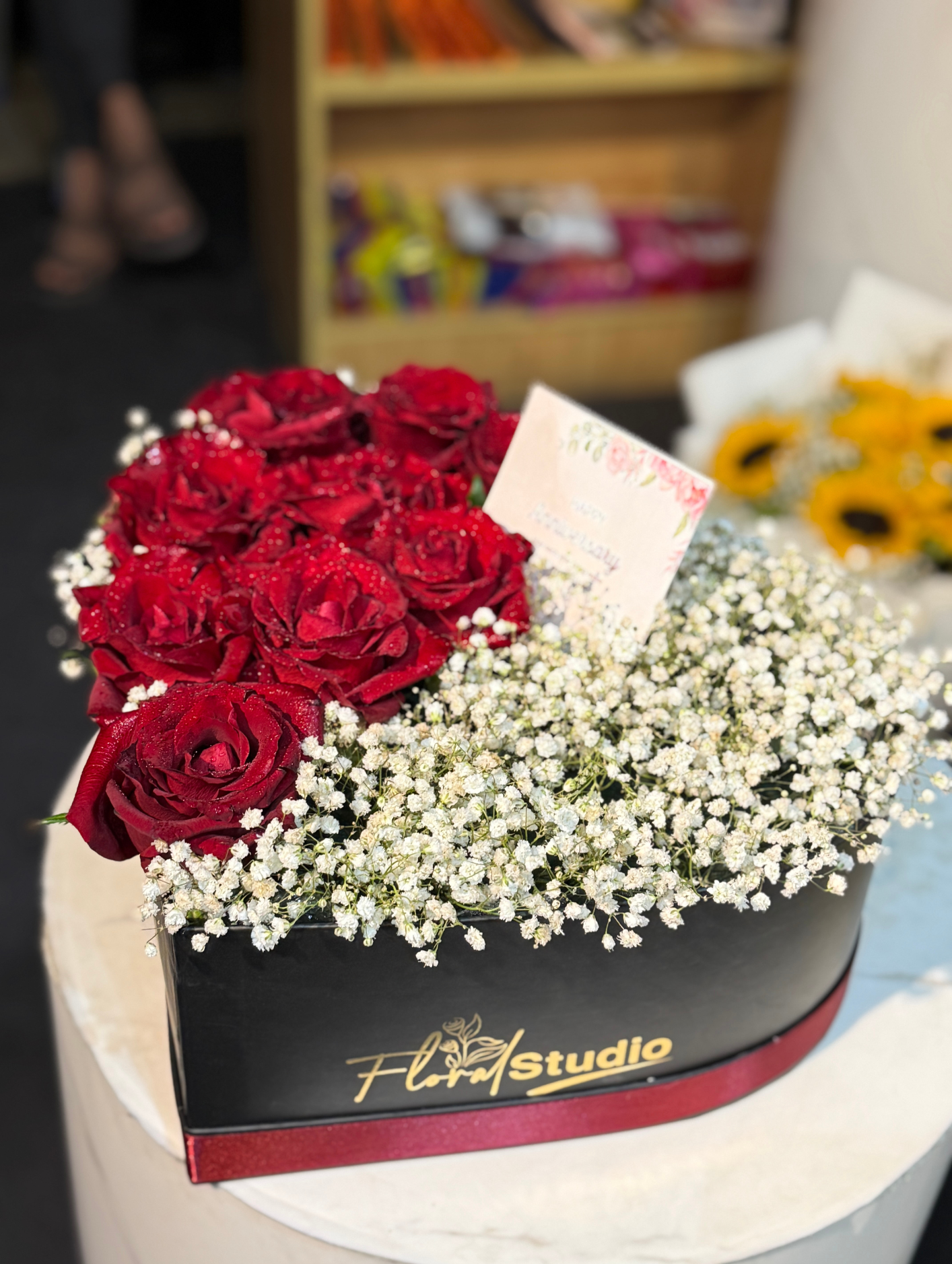 Heart-shaped black box with red roses and white baby’s breath arrangement, 'Blooming Love' by Floral Studio, perfect for romantic gifts.