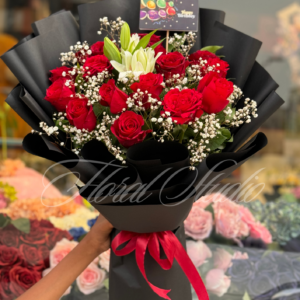 Crimson Charm bouquet with red roses, white lilies, and baby's breath wrapped in black paper with a red ribbon – ideal for special occasions.