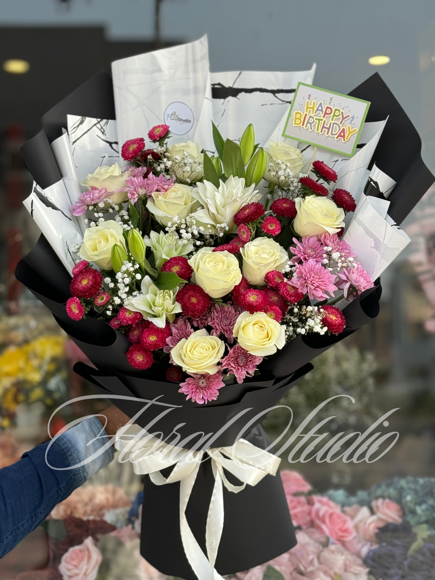 Floral Elegance bouquet featuring white roses, red daisies, pink chrysanthemums, and baby's breath, wrapped in stylish black and white marble paper with a white satin ribbon.