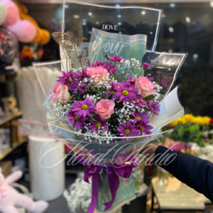 Vibrant flower bouquet featuring purple chrysanthemums, pink roses, white baby’s breath, and butterfly accents wrapped in transparent luxury packaging with a purple ribbon.