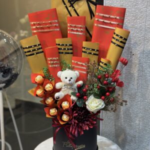 Golden Bliss Basket featuring Ferrero Rocher chocolates, a plush teddy bear, fresh flowers, and elegant gold and red packaging in a black box, perfect for gifting and available for online flower delivery in Lahore.