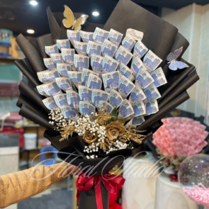 An opulent bouquet featuring carefully folded Pakistani currency notes, golden artificial roses, white baby's breath, and shimmering golden foliage, wrapped in elegant black paper and tied with a red satin ribbon, perfect for special celebrations and gifting.