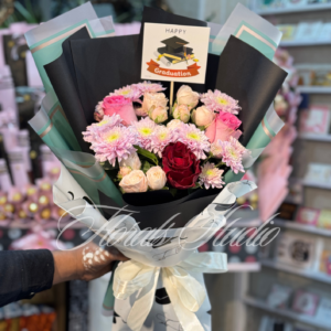 "Grad Bloom Elegance – Graduation bouquet with pink chrysanthemums, white roses, and red roses wrapped in black and white graduation-themed paper, available for fresh flower delivery in Lahore."