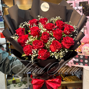 Red Symphony bouquet featuring fresh red roses and baby’s breath wrapped in black paper with a red ribbon – online flower delivery Lahore, Bahria Town florist.