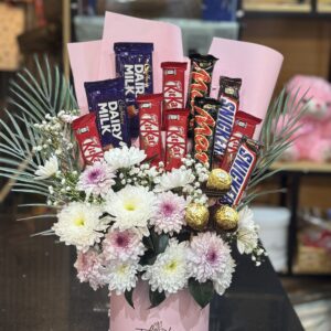 A luxury pink box with fresh white and pink chrysanthemums, baby's breath, and premium chocolates including KitKat, Snickers, Dairy Milk, and Ferrero Rocher. Perfect for gifting from a flower shop in Bahria Town, Lahore.