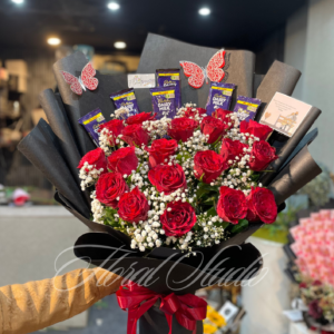 Sweet Scarlet Surprise bouquet featuring fresh red roses, white baby's breath, Cadbury Dairy Milk chocolates, elegant black wrapping with a red ribbon, and decorative butterfly accents, available for online flower delivery in Lahore.